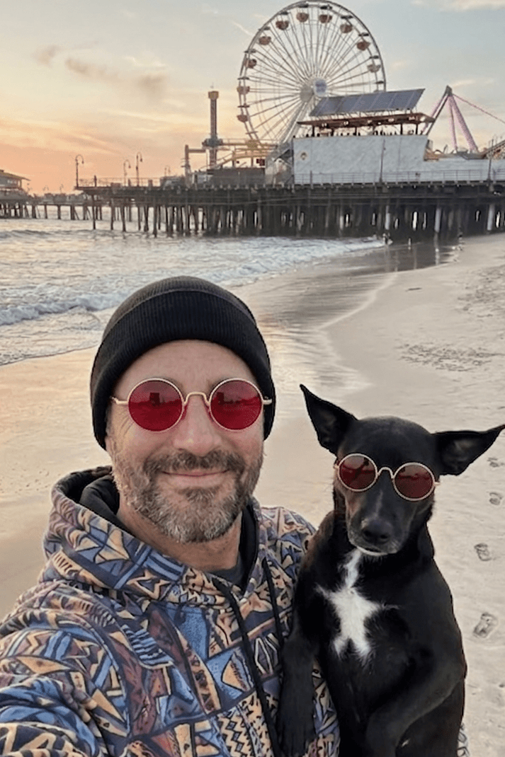 Man and dog wearing sunglasses on a beach with a Ferris wheel in the background